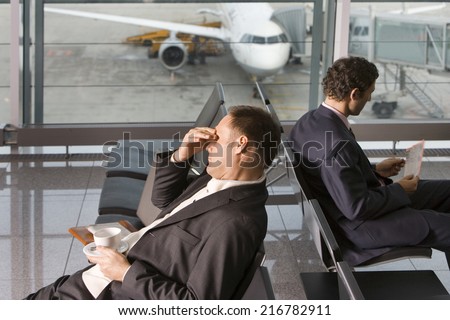 A man holding a cup rubbing his eyes in the airport.