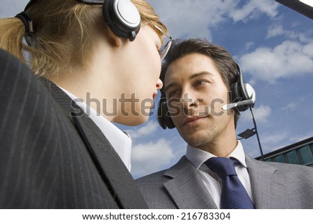 Two business people wearing headsets stand face to face.