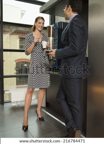 Two office people talking by the coffee maker.