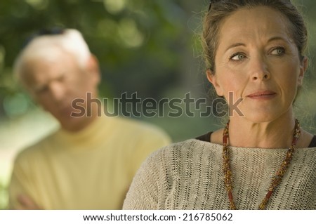A sad woman, man blurred in the background.