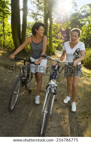 Two women walking with cycles.