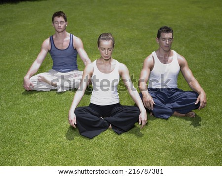 Young woman and two young men meditating on a lawn