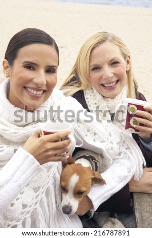 Portrait of two young women holding tea cups with a dog and smiling