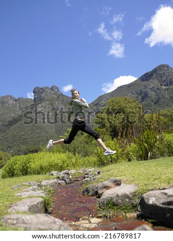 Side profile of a young woman jumping over a stream