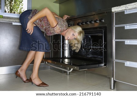 A woman bending to look at an oven.