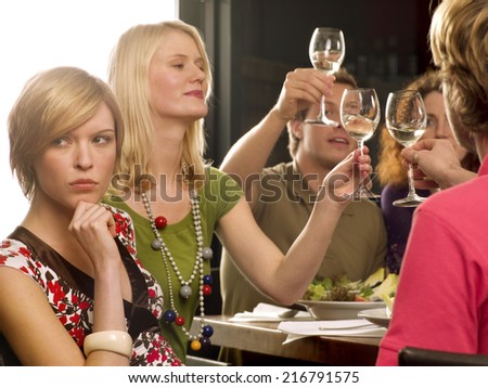Close-up of a young woman thinking with her hand on her chin and her friends toasting wine glasses in the background