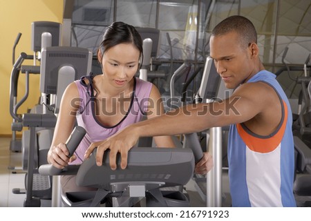 Trainer helping a woman with the cycle in a gym.