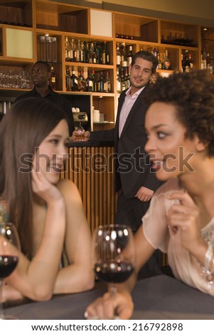 Women talking, man looking at them in the background.