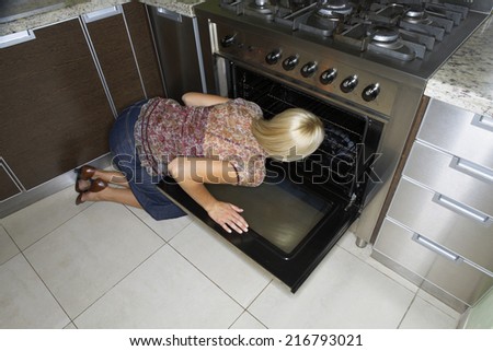 A woman kneeling down to look at an oven.