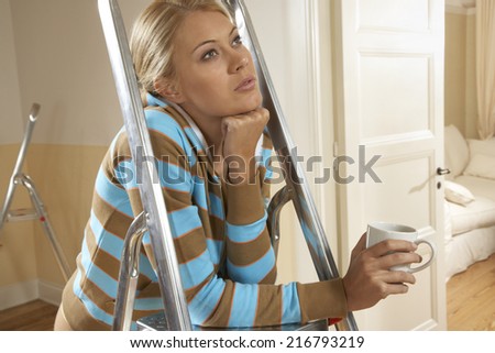 Close-up of a young woman leaning on a step ladder and thinking