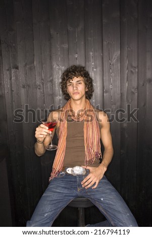 Young man sitting on a stool and holding a glass of cocktail