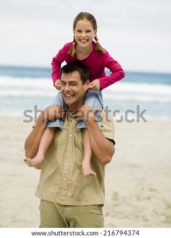 A daughter sitting on her fathers shoulders and pulling his ears.