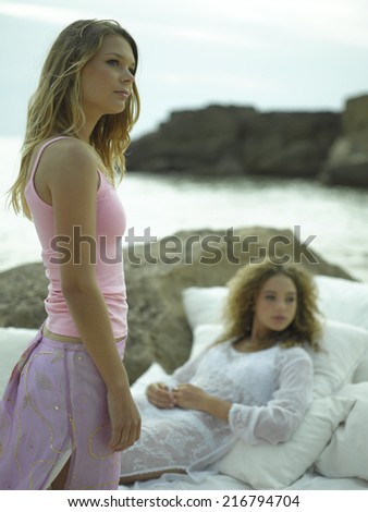 Side profile of a young woman standing with another young woman lying down