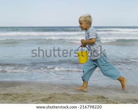 A boy running on the beach with a sand pail