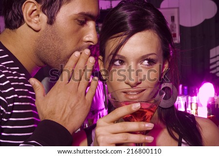 Man whispering into a young woman's ear in a bar