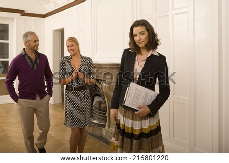 A real estate agent holding documents with a couple walking behind her