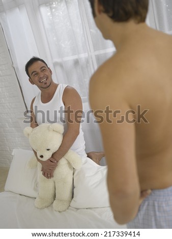 Young man kneeling on the bed and looking at another young man