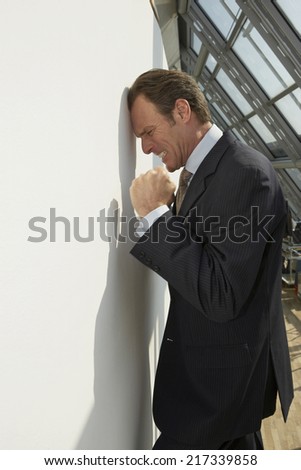 Side profile of a businessman leaning against a wall and looking irritated
