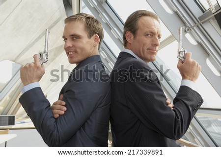 Two businessmen holding revolvers and standing back to back