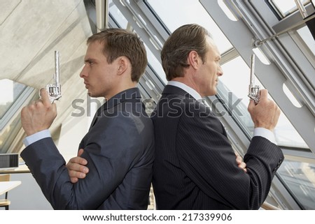 Two businessmen holding revolvers and standing back to back