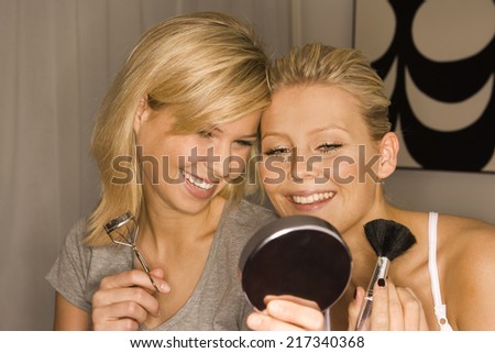 Close-up of two young women looking at a mirror and smiling