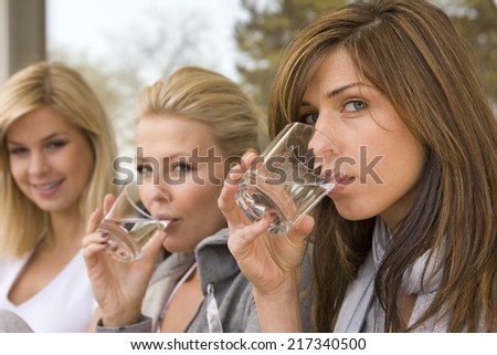 Portrait of two young women drinking wine and their friend smiling in the background