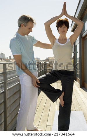 Woman practicing yoga, man standing beside her