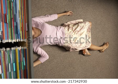 High angle view of a businesswoman lying under a filing cabinet drawer