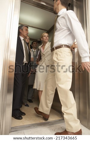 Side view of a businessman entering an elevator with four business executives in it