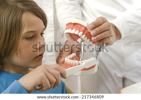 Dental assistant teaching a boy how to brush teeth