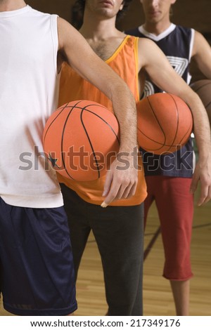 Three young men standing in a court and holding basketballs