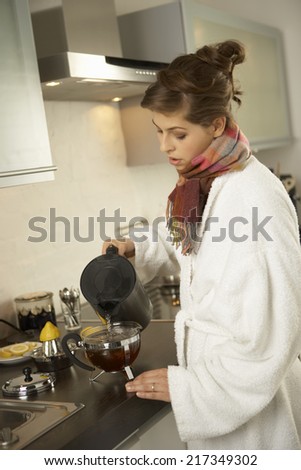Side profile of a mid adult woman pouring water into a container of herbal tea