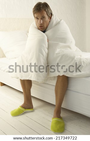 Portrait of a mid adult man wrapped in a duvet and sitting on the bed