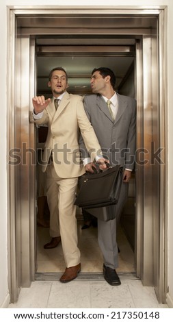 Two businessmen struggling to get out of an elevator