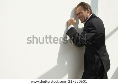 Side profile of a businessman leaning against a wall and looking irritated