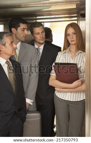 Three businessmen looking at a businesswoman standing in an elevator