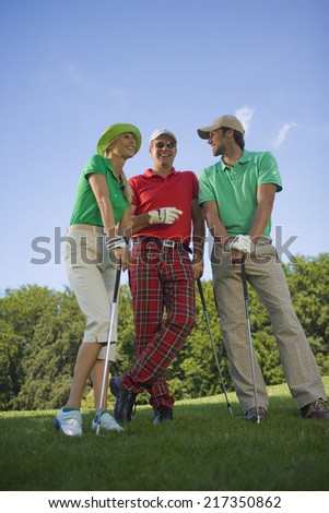Two mid adult men standing with a mid adult woman on a golf course and holding golf clubs