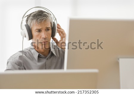 Businessman sitting in front of a desktop PC and listening to music