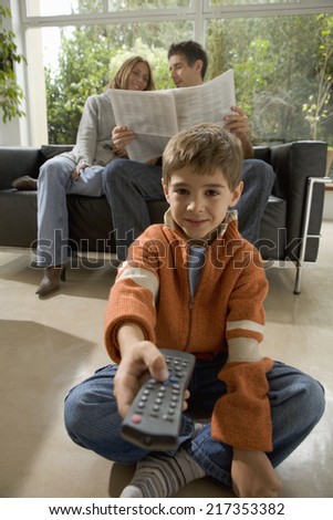 Boy with TV remote control and parents with newspaper in background