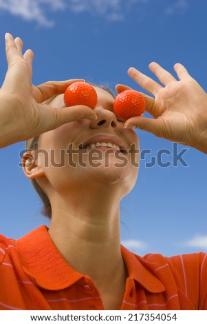 Close-up of a mid adult woman covering her eyes with golf balls and smiling