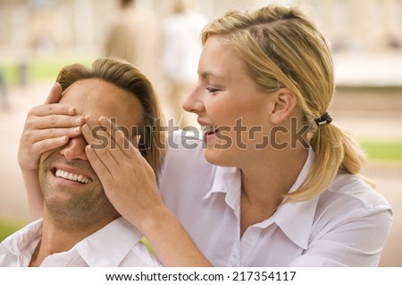 Close-up of a young woman covering a young man\'s eyes and smiling
