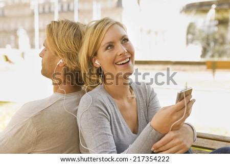 Close-up of a young couple sitting back to back and listening to an MP3 player