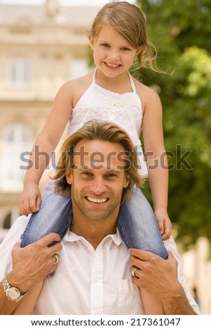 Portrait of a young man carrying his daughter on his shoulders and smiling