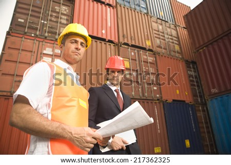 Portrait of a businessman and a dock worker standing in front of cargo containers
