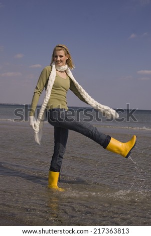 Young woman in winter clothing and boots splashing water at the beach