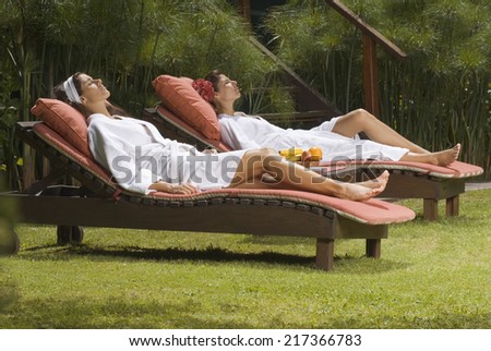 Side profile of two young women in bathrobes and resting on lounge chairs