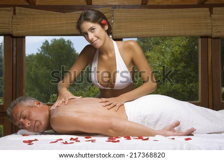 Side profile of a mature man receiving a back massage from a young woman massage therapist