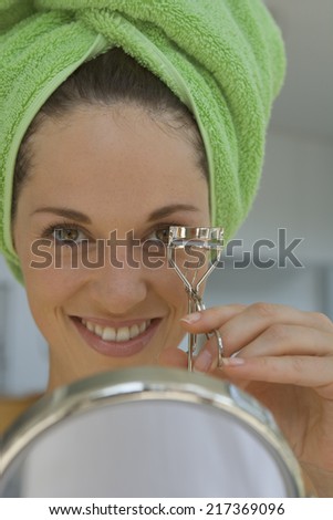 Woman with eyelash curler and hand mirror