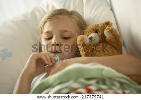 High angle view of a girl lying on the bed and measuring her temperature with a thermometer