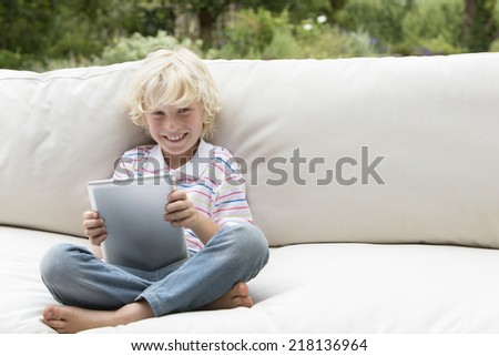 Portrait of smiling boy using digital tablet on outdoor sofa